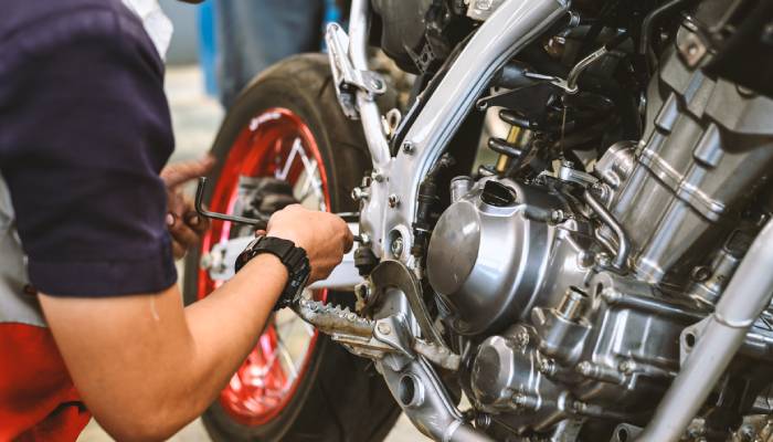 A service technician crouching and working on a motorcycle engine component with an Allen wrench in a garage.