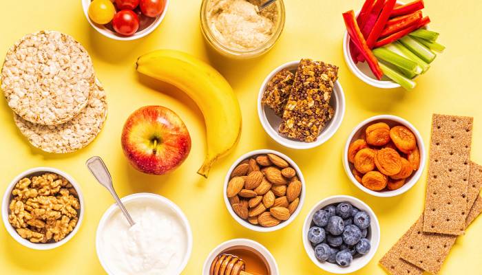 A variety of tasty, healthy snacks, including rice cakes, fresh fruit, bowls of almonds, honey, and yogurt.