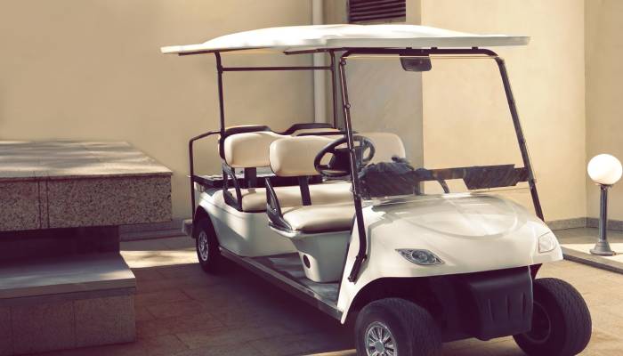 A white golf cart with two rows of seats is parked close to a building. It is in good condition and ready to sell.