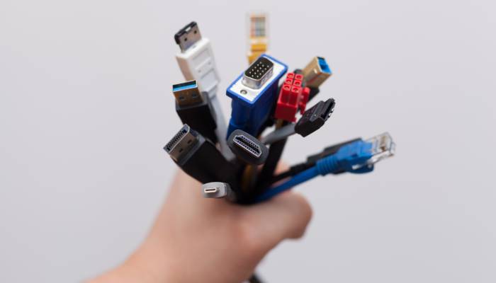 A hand is holding a whole bunch of different cables with various connectors. The background is white.