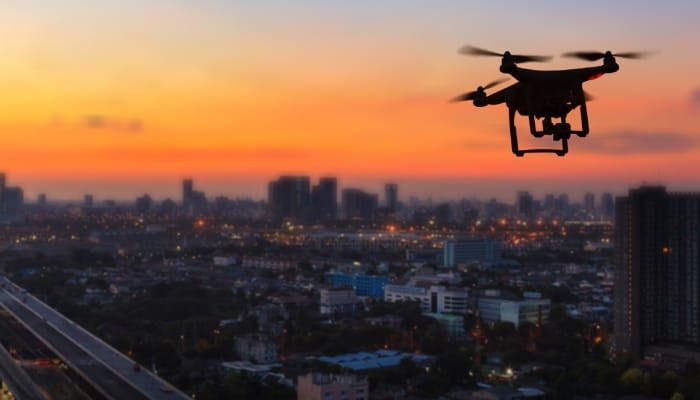 A drone is flying over a bustling cityscape and highway during a beautifully vibrant orange and yellow sunset.