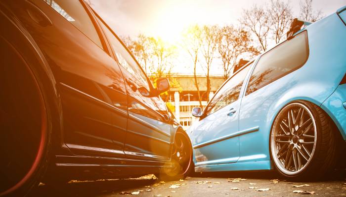 A low point-of-view of two modified street cars with high-end rims parked next to one another in a lot.