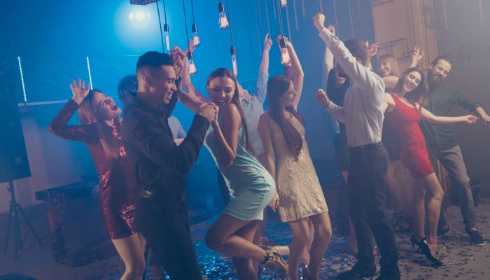 A group of young students at a school dance. Everyone is dressed in semi-formal wear and smiling, having a good time.