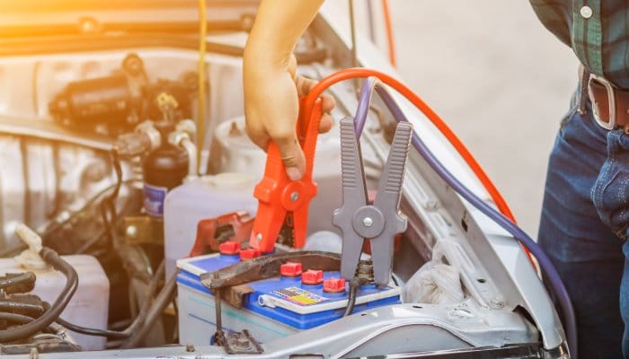 A boat owner at the dock charging the boat's battery. The boat is behind them as they attach jumper cables to the battery.