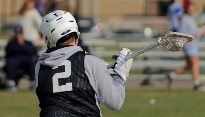 A young lacrosse player out on the field. He's wearing a black, number 2 jersey and holding a lacrosse stick.