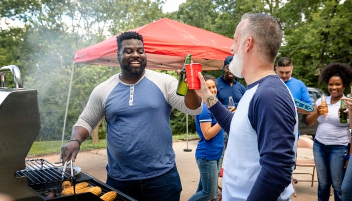 A group of friends smiling and cheering drinks at a tailgate party while grilling food and celebrating together.