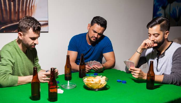 A group of men playing cards around a poker table. There are drinks and bowls of chips on the table.