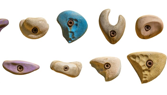 Twelve bolt-on climbing holds are arranged in two rows over a white background. They are different colors and shapes.