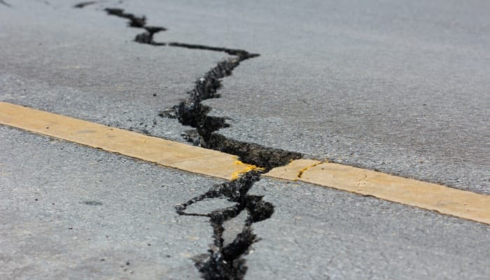 A crack from an earthquake runs through a road. The crack separates a yellow line that runs through it.