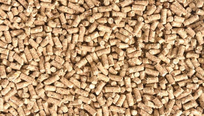 A close-up of granulated animal feed, consisting of light brown, uniformly sized, and log-shaped pellets.