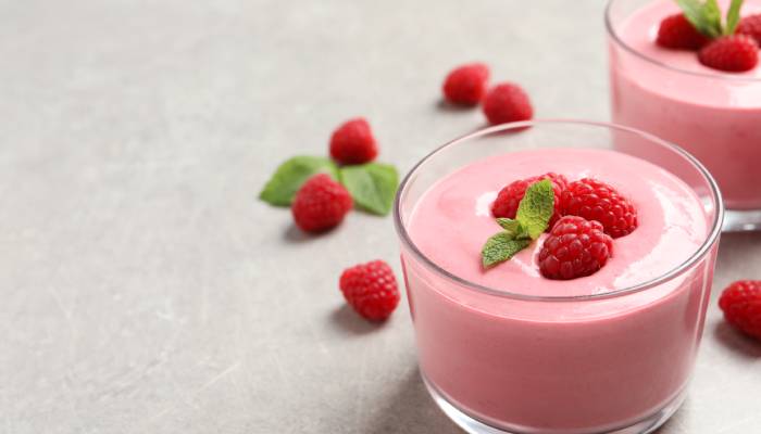 A perfectly pink raspberry mousse topped with three fresh raspberries and a sprig of mint, sitting on a countertop.