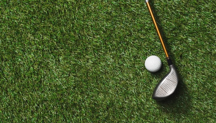 A bronze golf club and a white golf ball sitting on the putting green. The putting green is freshly groomed and healthy.