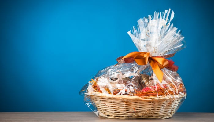 A wicker gift basket wrapped in plastic and tied with an orange ribbon against a blue background.