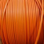 A close-up view shows a long, orange fiber optic cable wrapped around a large, light-colored wooden spool.