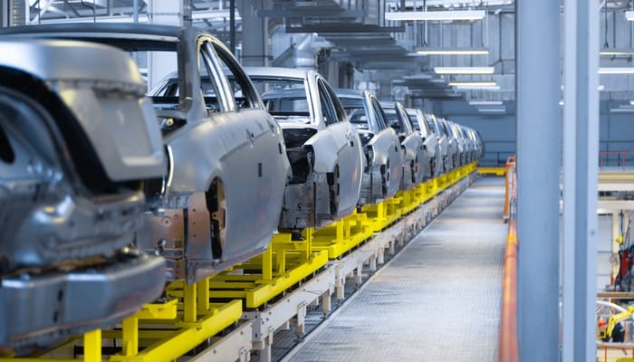 A production line of several vehicles in an automotive manufacturing facility. Each car looks the same, with no windows or tires.