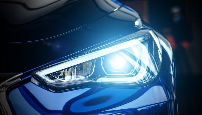 A close-up view shows the driver's side headlight of a dark-blue vehicle that's on. The background is dark.