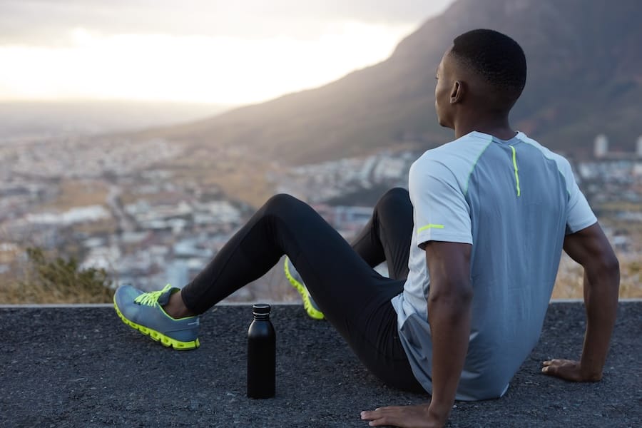 deep thoughts black man wears casual sportswear feels relaxed top poses back front mountain scenic view keeps hands asphalt has outdoor workout being fatigue lack strength