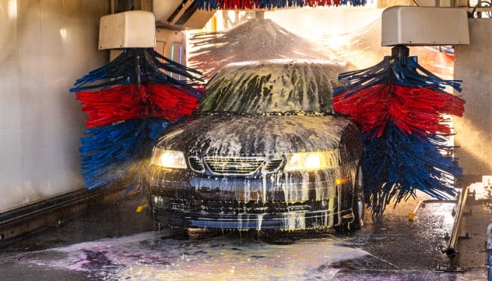A dark blue car going through an automatic car wash. Red and blue scrubbers cover the vehicle in a soapy solution.