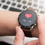 A health-monitoring smartwatch shows a heartbeat symbol and numbers next to a red arrow and a green arrow.