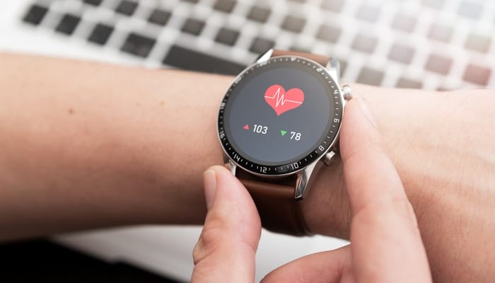 A health-monitoring smartwatch shows a heartbeat symbol and numbers next to a red arrow and a green arrow.