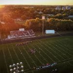 An aerial view of a football game at sunset, showing fans in the stands and a running track around the field.