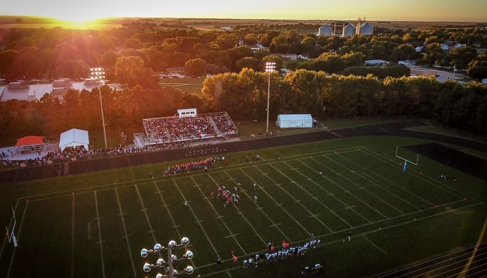 An aerial view of a football game at sunset, showing fans in the stands and a running track around the field.