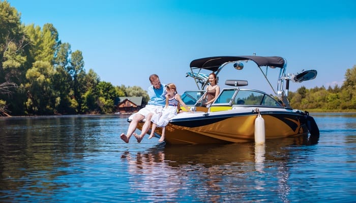 A father and daughter sit on the bow of a yellow and black motorboat while the mother stands behind the wheel.