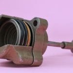 A close-up of an old dirty turbo actuator and its internal parts isolated against a purple-pink background.