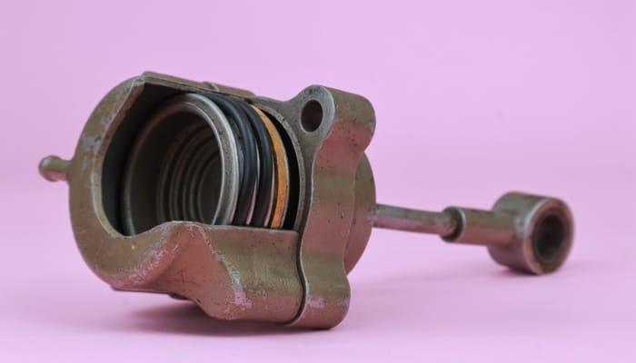 A close-up of an old dirty turbo actuator and its internal parts isolated against a purple-pink background.