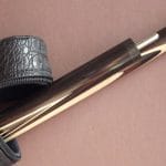A brown pool cue sticking out of a leather carrying case. The cue has been split in two for transportation purposes.