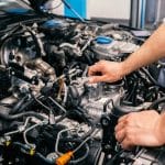 A person leans on the various exposed vehicle parts that are under the hood. The hood is propped open.