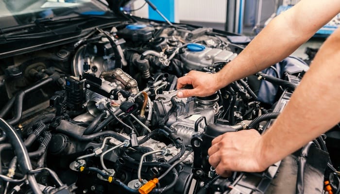 A person leans on the various exposed vehicle parts that are under the hood. The hood is propped open.