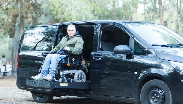 A hydraulic mechanism lifts a man sitting in a wheelchair into a black van. His back is facing the van's interior.