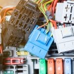 A colorful wire harness surrounded by many automotive connectors. The connectors vary in size and color.