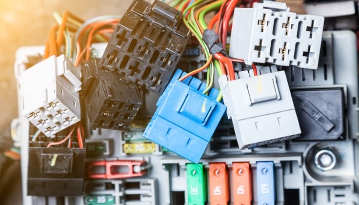 A colorful wire harness surrounded by many automotive connectors. The connectors vary in size and color.