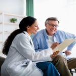 A man and a woman are sitting next to each other. The woman is holding a clipboard that the man is looking at.