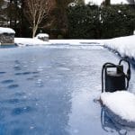 An in-ground pool covered with a layer of frozen water, surrounded by several inches of snow in the winter.